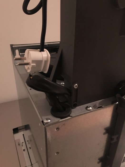 Köksfläkt med synligt skadat svart plasthölje och klämd sladd nära elektriskt uttag.