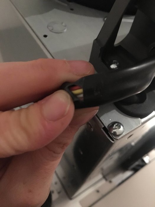 Närbild på en hand som håller en skadad sladd med brutet plasthölje från en köksfläkt.