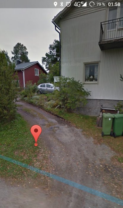 Grusväg som svänger vid vit husknut, röd stuga i bakgrunden, gröna soptunnor vid vägen.