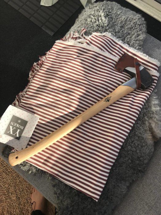 Yxa med trähandtag och läderskydd på ett randigt tyg, köpt på en bruksmarknad.