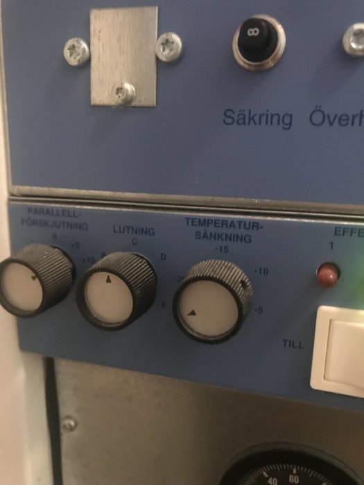 Närbild av kontrollpanel med vred för temperatursänkning och parallellförskjutning samt säkringsknapp.