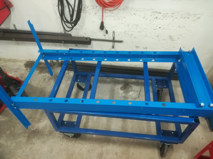 Delvis monterad blå arbetsbänk i ett verkstadsutrymme, saknar några komponenter.