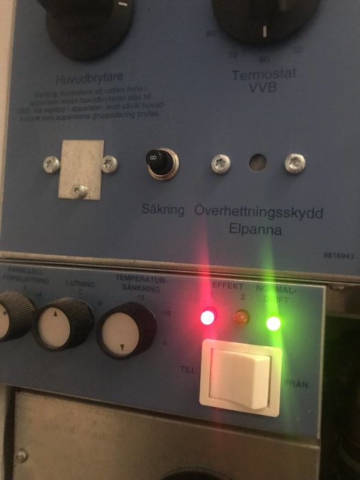 Kontrollpanel med två knappar, öppet plastlock, etikett 'Överhettningsskydd', tända effektlampor.