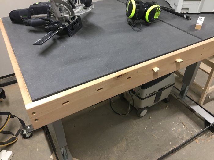 Svart mdf-arbetsbord med aspram och integrerade domino-hål, elektroniskt höjdjusterbart underrede.