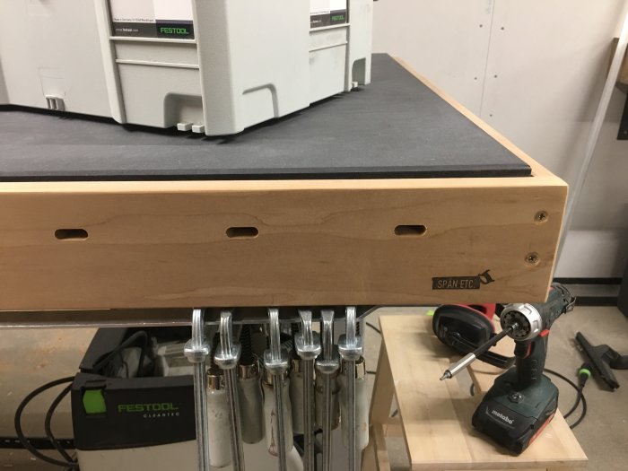 Arbetsbord med svart skiva på asp-underrede och frästa domino-hål, tillsammans med verktyg och Festool-produkter.