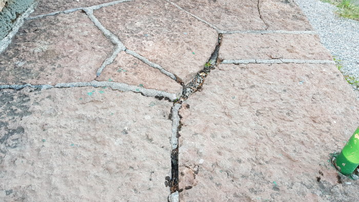 Slitet Ölandsten-stensättning med skadade och övervuxna fogar mellan stenplattorna.