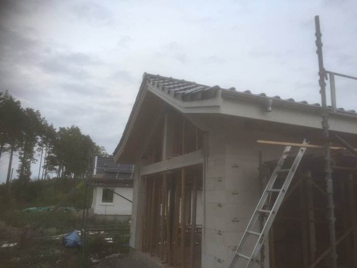 Hus under konstruktion med nyinstallerade gavelpannor på taket mot en molnig himmel.