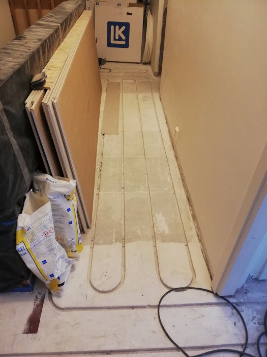 Installation av golvvärme med synliga värmerör och isoleringsplattor längs en korridor under renovering.