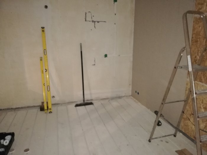 Ofärdigt rum under renovering med exponerade väggar, en stege och en gul vattenpass vid väggen.