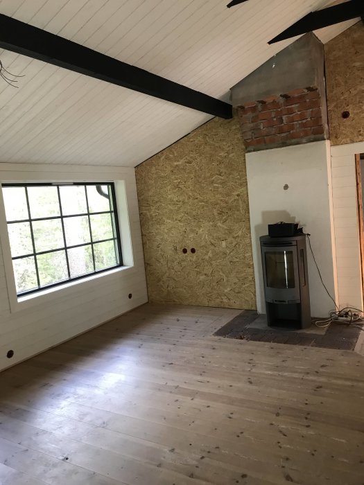 Renoveringsprojekt med en hall med massiva trägolv, OSB-väggpanel och en braskamin mot en tegelbakgrund.