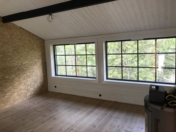Renoverad hall med nytt golv och väggpanel, stor fönster utanför synlig, oskyddade takbjälkar.