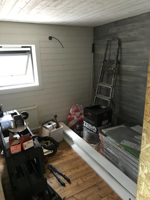 Renoverad hall med nya väggpaneler, byggmaterial och stegar under konstruktion.