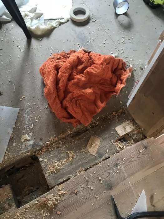 Ett uppbrutet golv med ett orange badlakan som används som isolering, omgivet av byggavfall och verktyg.