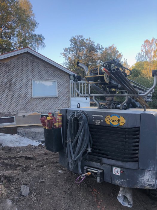 Borrigg framför hus under renovering med synlig bergrund och nytt köksavloppsrör.