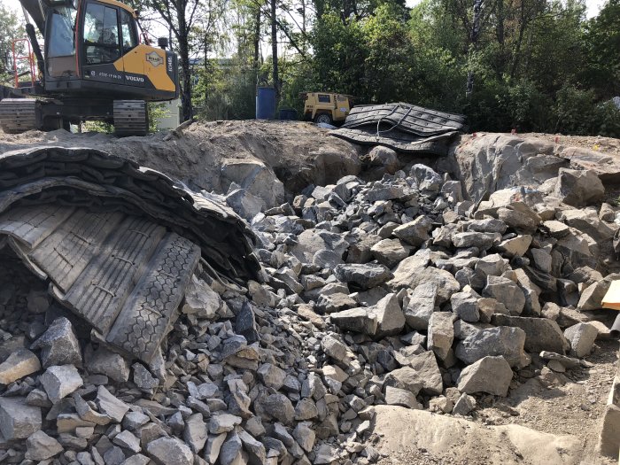 Grävmaskin bredvid hög med bruten bergsten vid husgrund under en tillbyggnadsprocess.