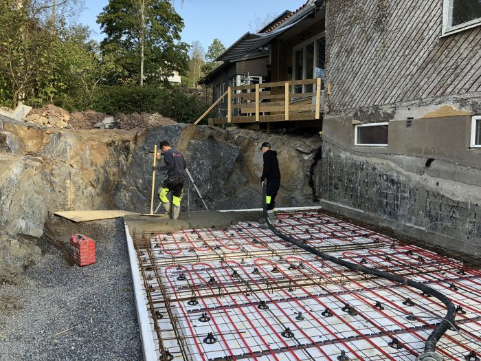 Arbetare häller betong över armeringsjärn vid grundläggning utomhus nära hus.