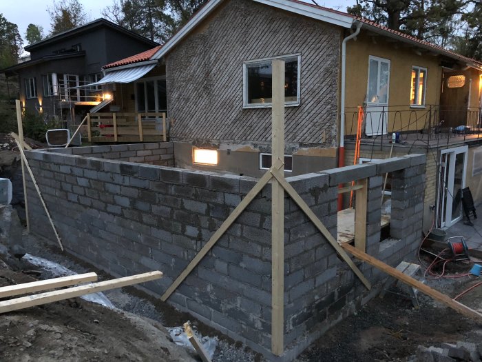 Nybyggda lecakällarväggar med pågående arbete och hus i bakgrunden i skymning.