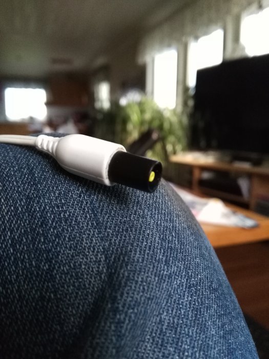 Elektrisk kontakt till en stötmaskin i fokus framför suddig vardagsrumsbakgrund.