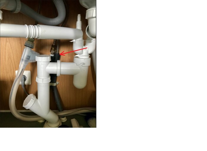 Under diskbänken med VVS-installationer och röd pil som pekar på vattentillförselsslangar.