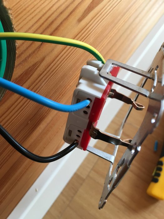 Elektrisk anslutning med färgade kablar kopplade till en väggmonterad eluttagsklämma.