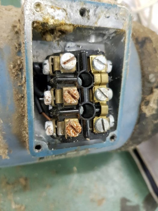 En öppnad elmotors anslutningslåda med synliga, korroderade skruvanslutningar och ledningar.