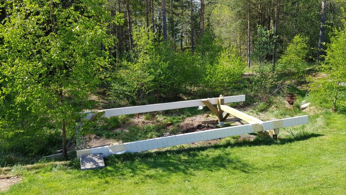 Grundkonstruktion av friggebod med träbalkar direkt på betongplintar i en skogsmiljö.