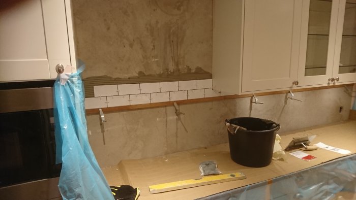 Kök under renovering med omonterade kakelplattor och verktyg på bänkskivan.