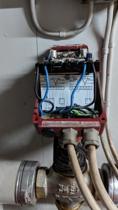 Öppen shunt med elektriska kopplingar och schematisk diagrametikett monterad på rör i ett värmesystem.