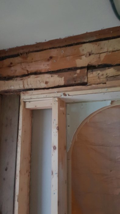 Bjälklag och stående stock med bult i hörnet av rum som väntar på renovering.