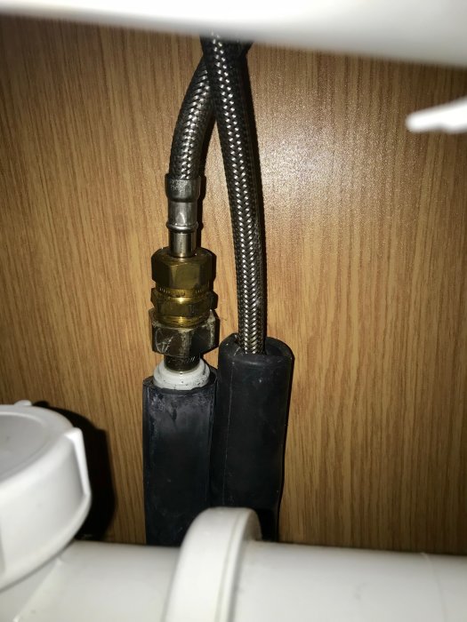 Två flexibla kranslangar anslutna till muttrar för varmt och kallt vatten, numrerade 10, under en handfatsskåp.