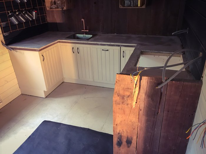 Kök i renovering med vita skåp och slipad skiva av cortenplåt på överhänget och sockeln.