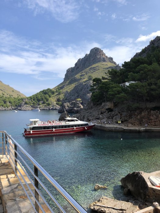 Vy över en klarblå vik på Mallorca med en turistbåt och berg i bakgrunden