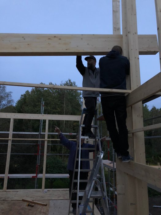 Personer uppför en träkonstruktion för en tillbyggnad med olika höjder i skymningen.