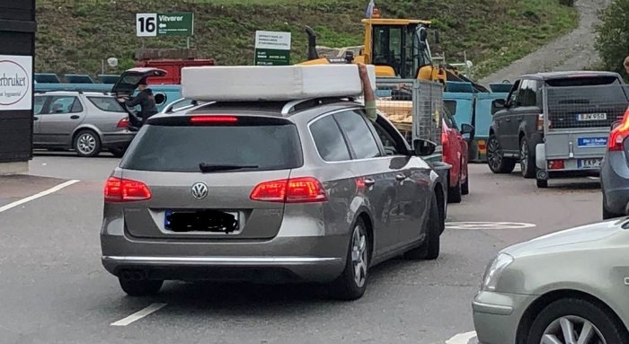 Grå Volkswagen med en stor madrass fastsäkrad på taket, står i kö på en återvinningsstation.