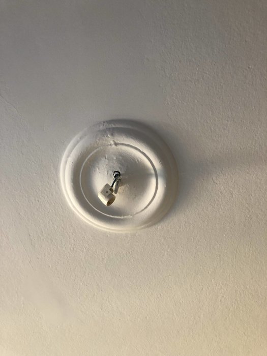 Gipstak med krona och utstickande krok för lampa, orört och redo för installation.