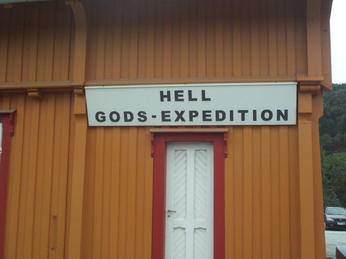 Skylt med texten "HELL GODS-EXPEDITION" på en gul stationsbyggnad.