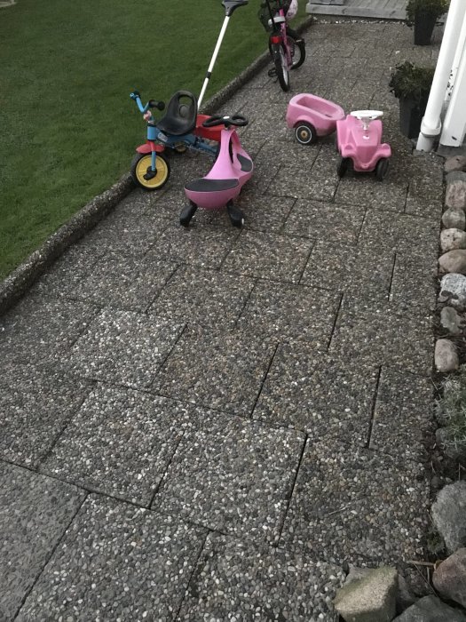 En gångväg med sjöstensplattor framför en dörr med barnleksaker spridda runtom.