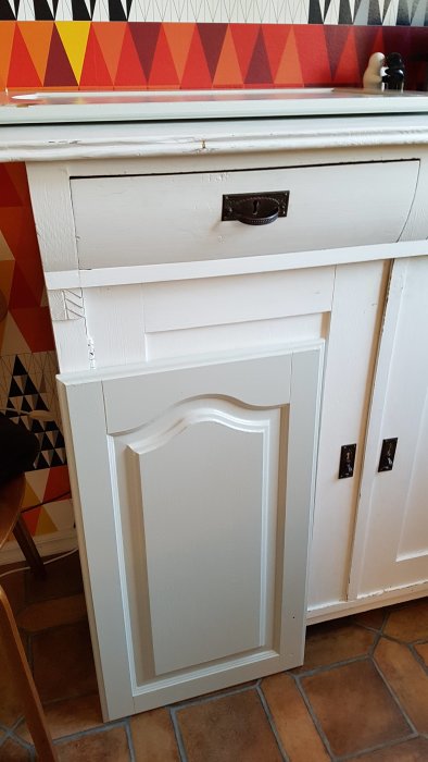Vitmålad kökslucka med pärlgrå linoljefärg och svart metallhandtag.