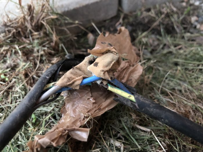 Improviserad kabelskarv utomhus med tejp och en trasig handskbit, med synliga koppartrådar och isolering.