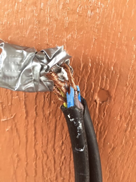 El-kabel skadad av häcksax lagad med tejp mot en brun vägg.