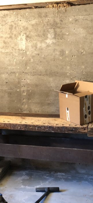 Oputsad källarvägg med synlig betong och en tom kartong på en brädhög, diskussion om putsning.