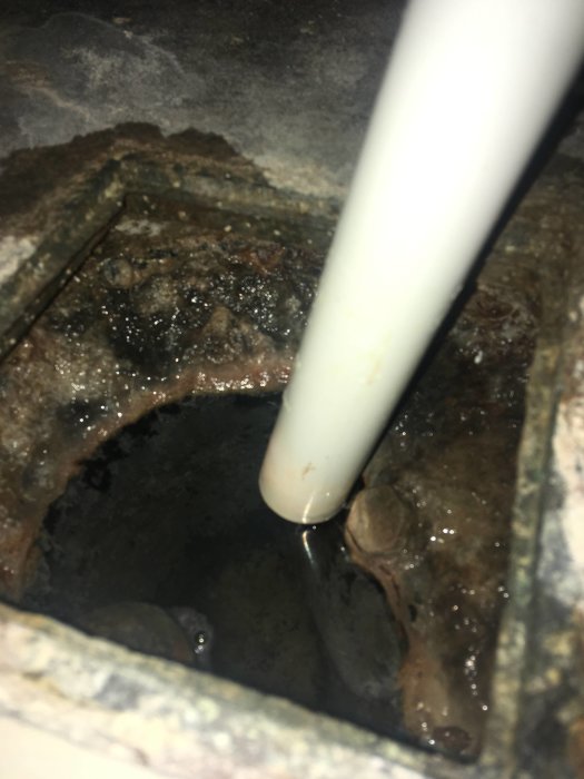 Avloppsrör och smutsig avloppsbrunn under en dusch, med synliga avlagringar och vatten.