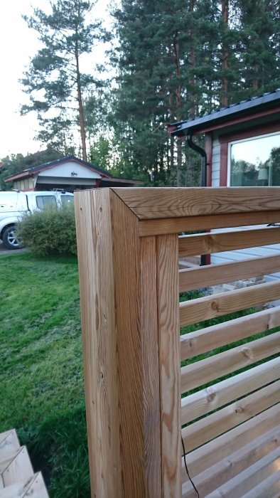 Nybyggt trästaket med horisontella plank framför ett bostadshus och träd.