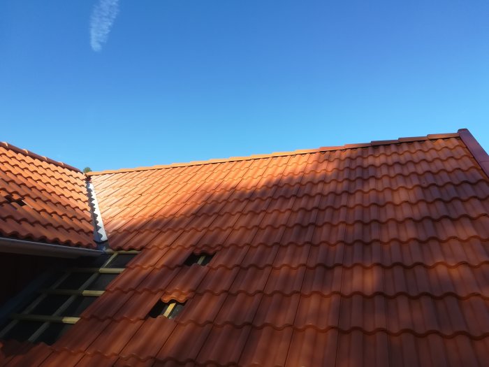 Nylagt tak med tegelpannor och plåtarbeten vid nock och gavel under klarblå himmel.