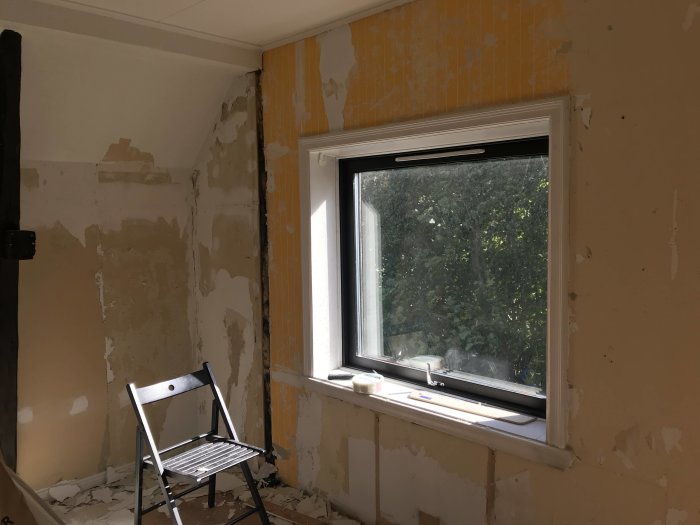 Renoveringsarbete i gammalt rum där knottrig tapet tagits bort, med stege vid fönster.