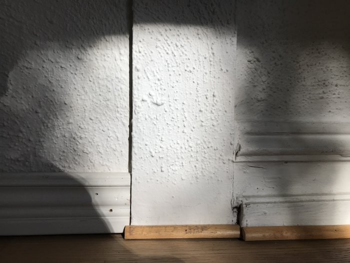 Gammal knottrig tapet och snickeridetaljer i ett äldre hus som fångar solljus och skuggspel.