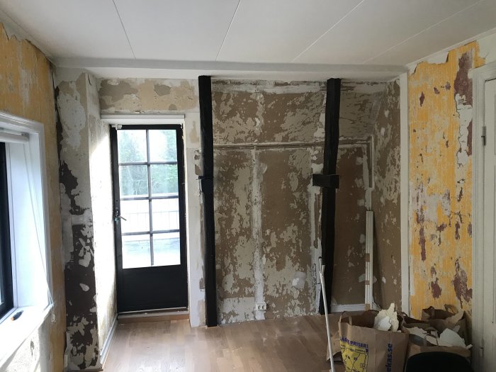 Renoveringsrum med delvis borttagna tapeter, synliga väggdetaljer och renoveringsmaterial på golvet.
