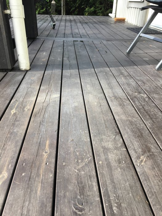 Slitet svartmålat trädäck med smuts och flammiga områden trots underhåll, nära sittmöbel och kwastskaft.