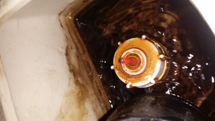 Överfylld toalett med synlig röd spolknapp och borttagen flottör mot kalkiga innersidor.