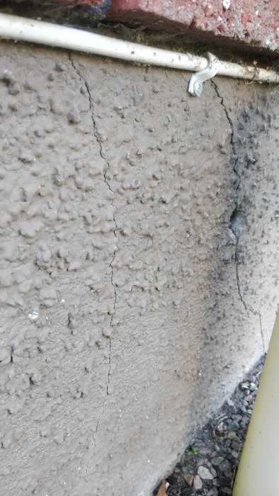 Spricka i en hussockel med synligt hål nära isolerrör och tegelkant ovanför.